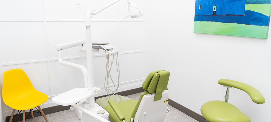 Pediatric dental exam room with green chairs and clean white walls.